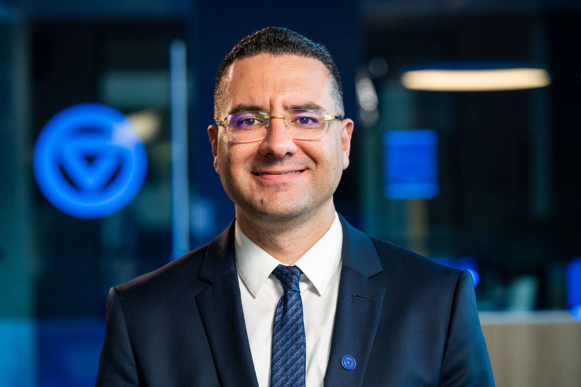 Dr. Marouane Kessentini, Dean of the College of Computing at Grand Valley State University, wearing a dark suit and tie, smiling in front of a blurred background with the GVSU logo glowing in blue.